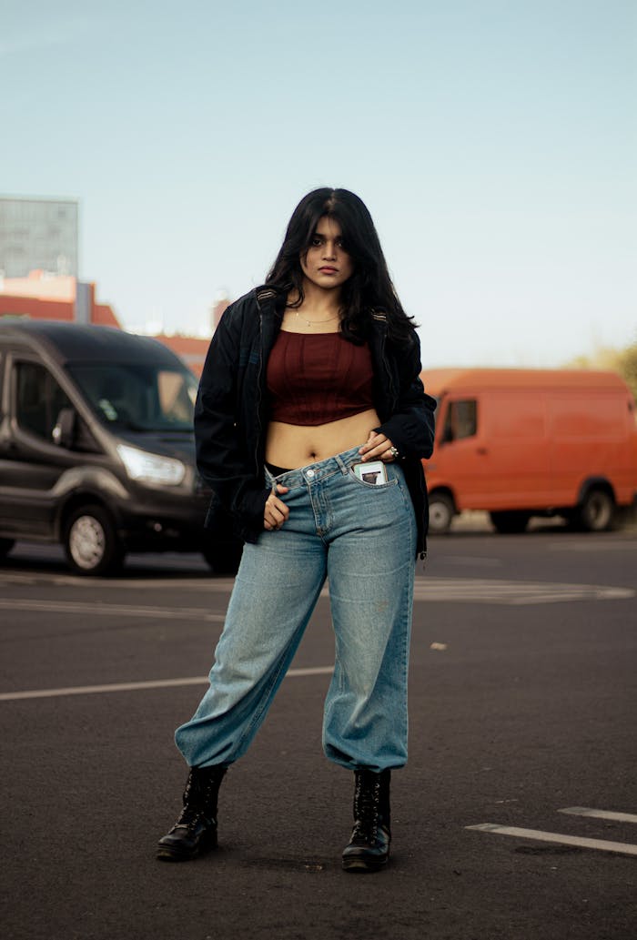 Home Young woman in casual wear posing confidently in a parking lot, showcasing urban fashion.