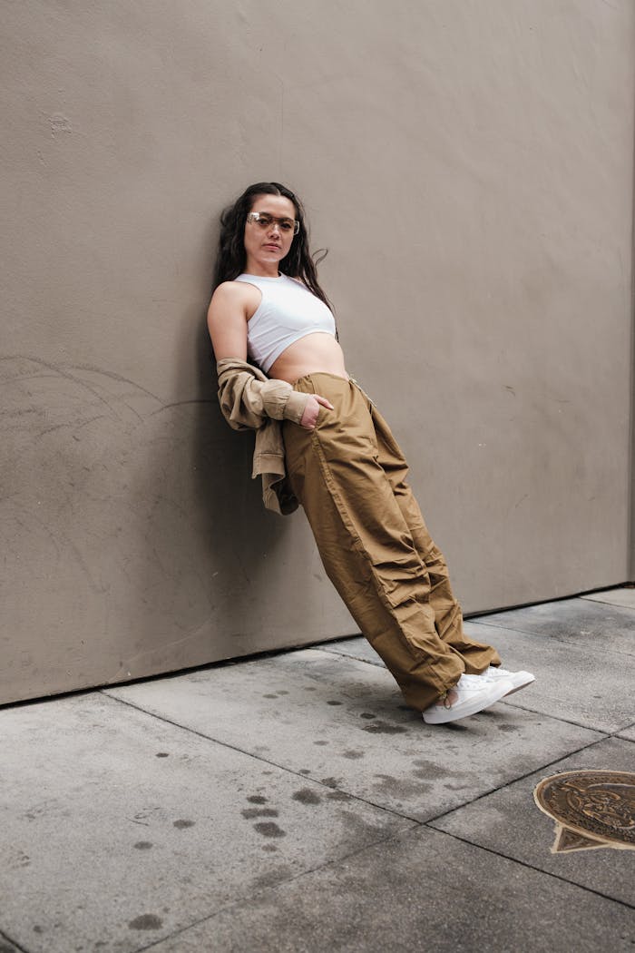 Woman poses in streetwear fashion against a minimalist wall, embodying modern urban style.